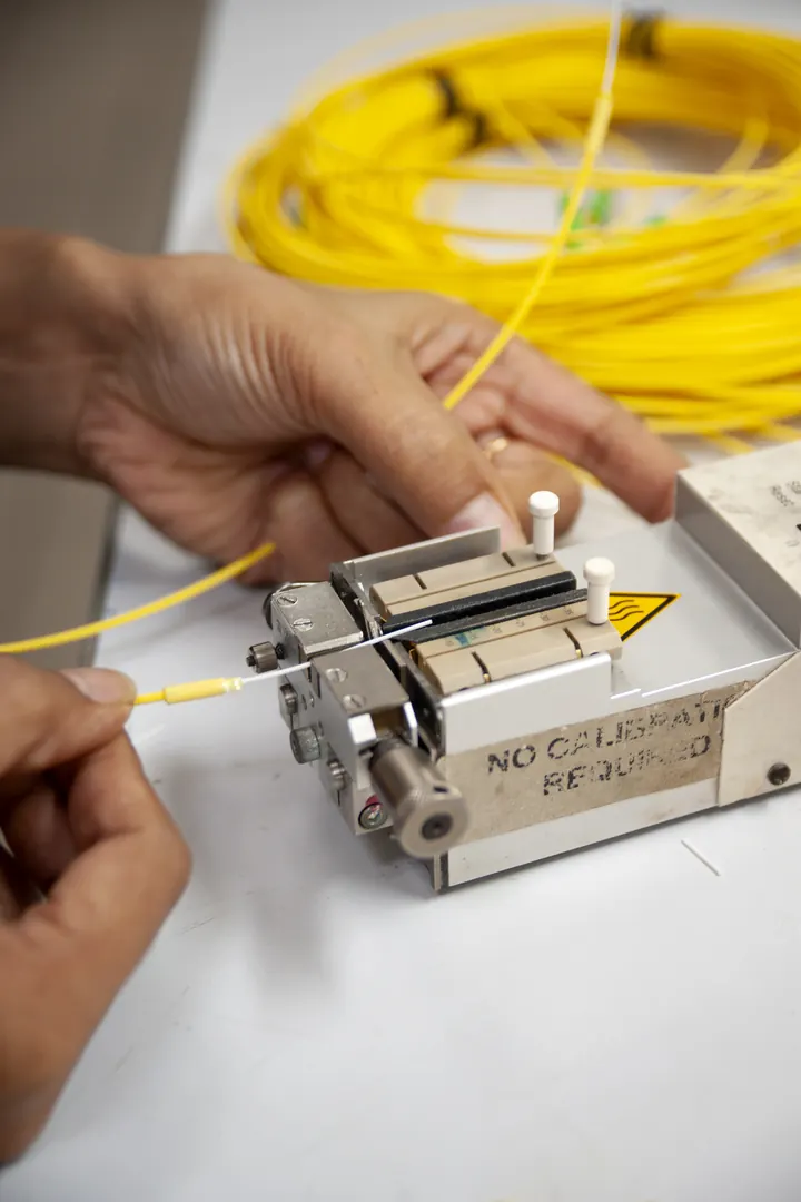 Mãos a fazer splicing de fibra ótica numa mesa de trabalho